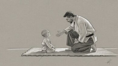 An instructor kneeling on the mat and reaching out a hand to a very young student sitting at eye level