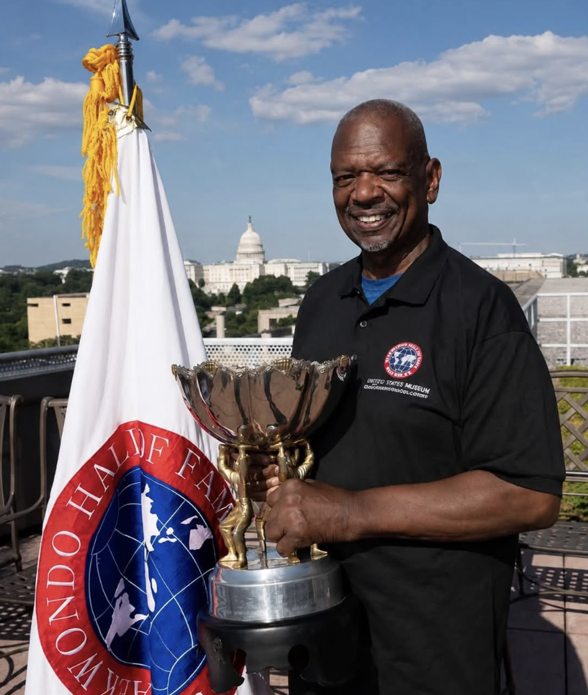 Great Grandmaster Albert Cheeks holding a large silver trophy on a rooftop in Washington DC with the Capitol dome visible behind him