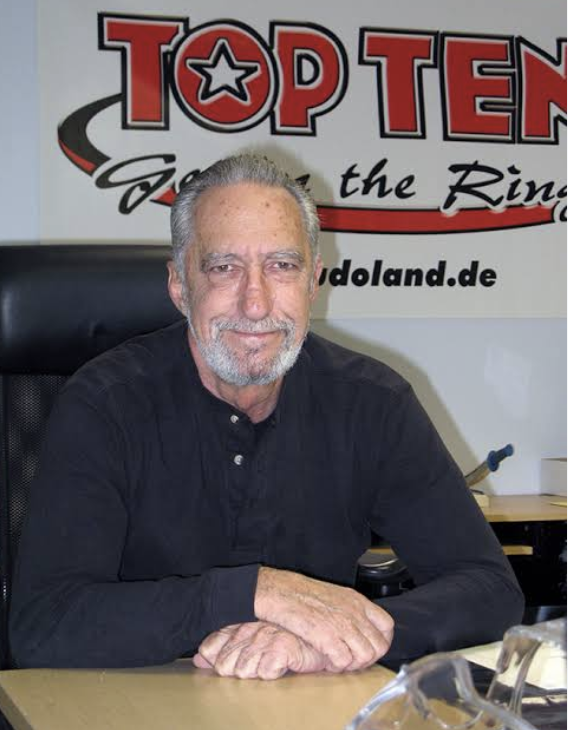 Mike Anderson on his 83rd birthday, seated in front of a Top Ten banner