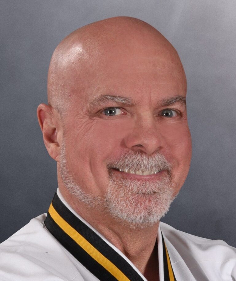Chief Master Greg Moody, Ph.D., smiling, in his Black Belt uniform