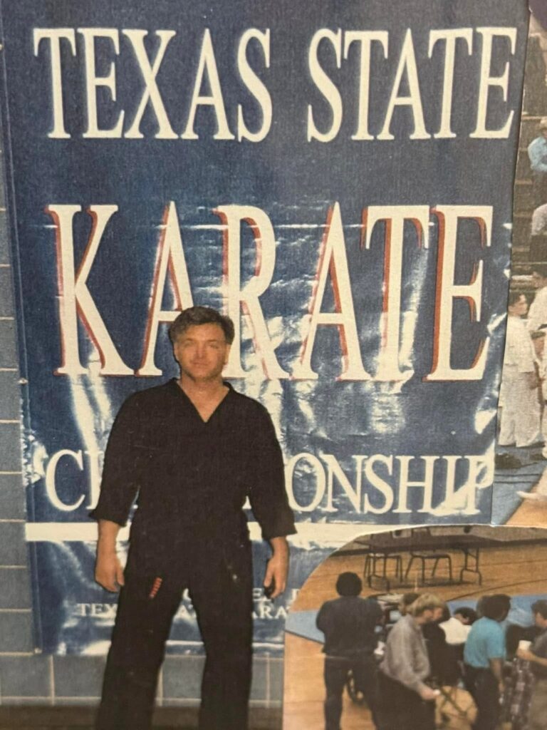Stephen Oliver in a black uniform standing in front of a Texas State Karate Championship banner on the set of Walker, Texas Ranger